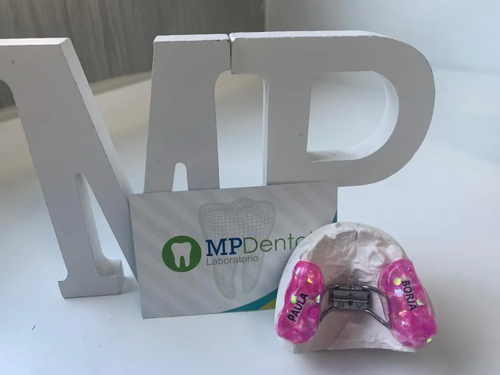 Aparato de ortodoncia rosa junto a las letras MP del laboratorio